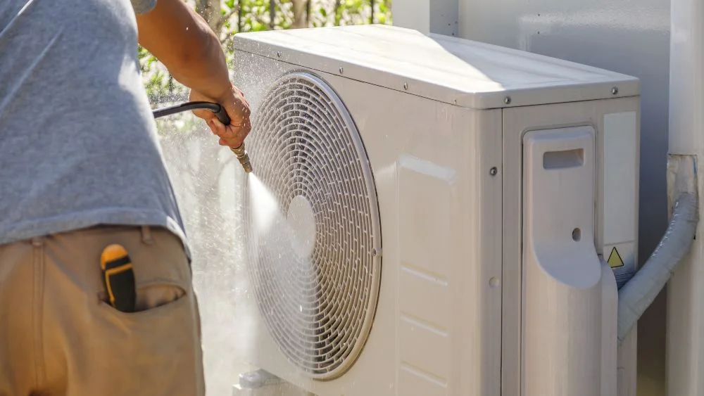 a man cleaning ac outdoor unit