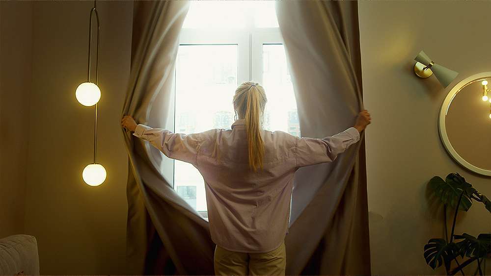 A woman opening curtains to let the sun in