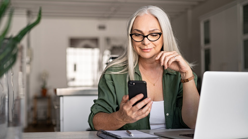 A woman using her phone to adjust AC settings. With smart thermostats, you can make changes from anywhere, which makes hem worth investing in.