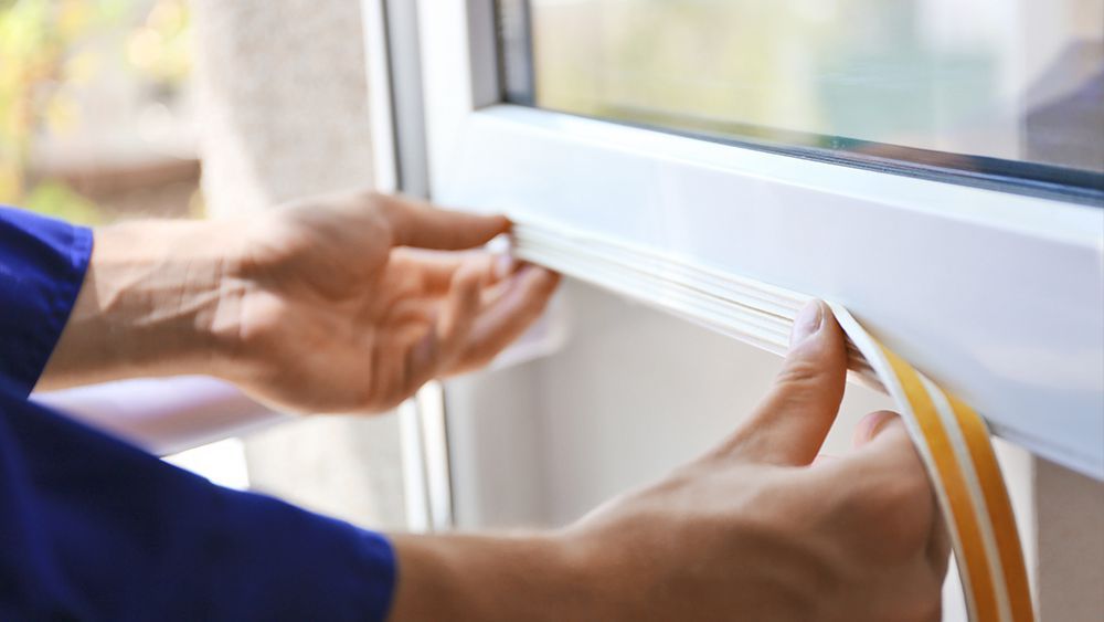 A man installing weatherstripping on the window